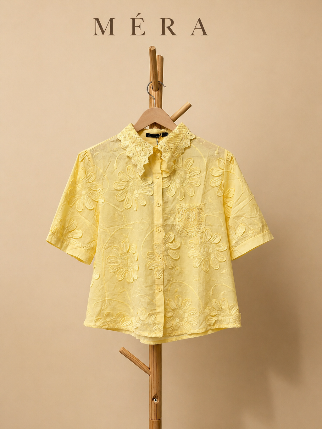 Yellow short-sleeve shirt on a wooden hanger against a beige background with 'Méra' branding.